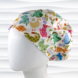 May include: A white scrub cap featuring a colorful pattern of whimsical animals and floral elements. The design includes rabbits, ducks, and other creatures in shades of pink, green, yellow, and blue. The cap is made of a soft fabric and has a small tag.