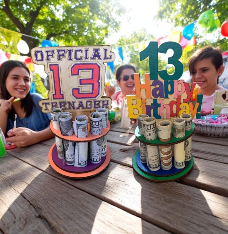 Może przedstawiać: Dwupoziomowe drewniane uchwyty na pieniądze z rolowanymi banknotami. Jeden uchwyt ma napis "OFFICIAL 13 TEENAGER". Drugi ma napis "13 Happy Birthday!". Uchwyty znajdują się na drewnianym stole z ludźmi w tle.