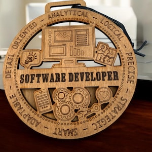 May include: A round, wooden plaque with the words "SOFTWARE DEVELOPER" in the center. The plaque features laser-cut graphics of a computer monitor, gears, and other tech-related symbols. The words "ANALYTICAL", "LOGICAL", "PRECISE", "STRATEGIC", "SMART", and "ADAPTABLE" are also included.