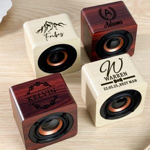 Può includere: Quattro altoparlanti cubici in legno personalizzati. Due sono di colore chiaro con componenti neri e due sono in legno scuro. Ogni altoparlante ha un design e un testo incisi unici.
