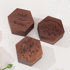 Pode incluir: Uma caneca de cerâmica branca com uma alça preta e o texto "But First, Coffee" em negrito preto. A caneca está sobre um fundo desfocado, sugerindo um ambiente acolhedor.