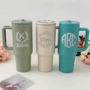 May include: Three personalized insulated tumblers in sage green, cream, and teal. Each tumbler features a handle, lid, and custom text: "Kelvin" with a laurel wreath, "Olivia" with floral accents, and "ABC" in a circular design.