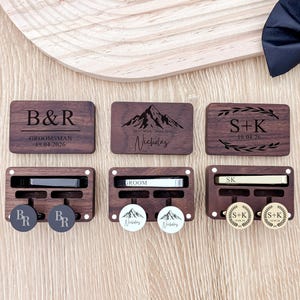 May include: A collection of personalized wooden groomsmen gifts. The set includes engraved boxes, tie clips, and cufflinks. The boxes feature initials, dates, and titles like "Groomsman" and "Groom." The cufflinks have initials and mountain designs.