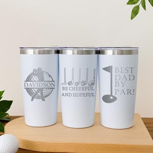 May include: Three white insulated tumblers with silver lids, each featuring golf-themed designs. One tumbler has a golfer graphic and the name "Davidson", another reads "Be Cheerful and Hopeful", and the last says "Best Dad by Par!"