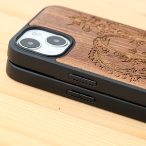 May include: A brown wooden phone case with a black protective bumper. The case has an intricate design carved into the wood. The case is designed for an iPhone with a dual camera system.