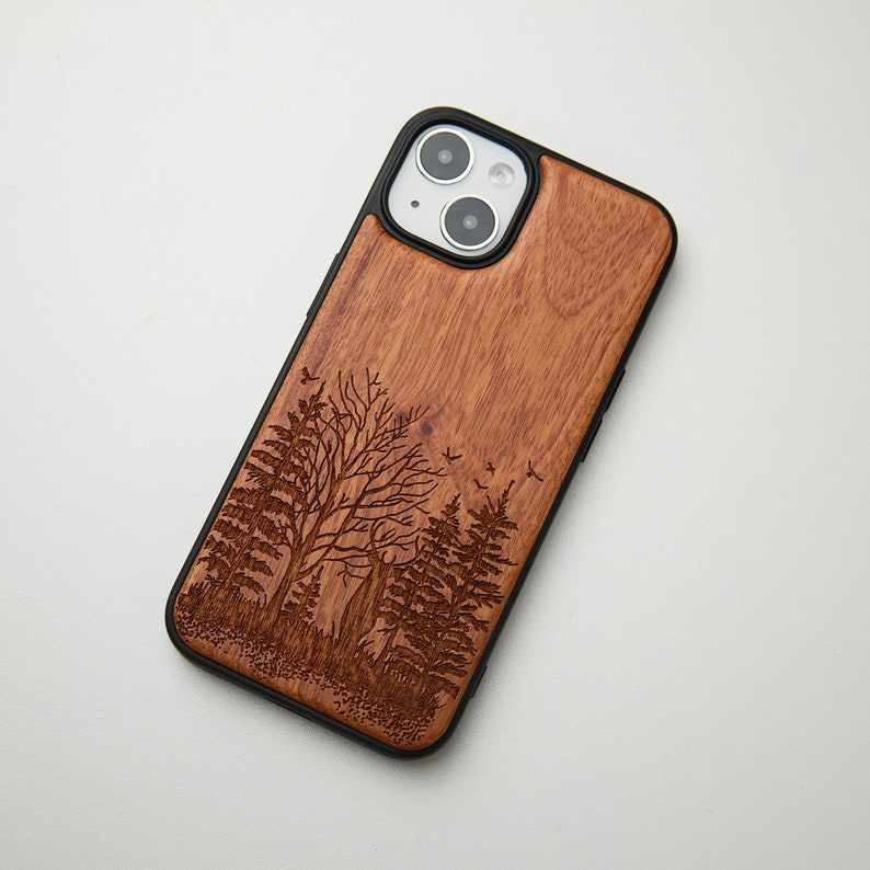 May include: A wooden phone case with a laser-engraved design of trees and birds. The case is black and has a natural wood finish.