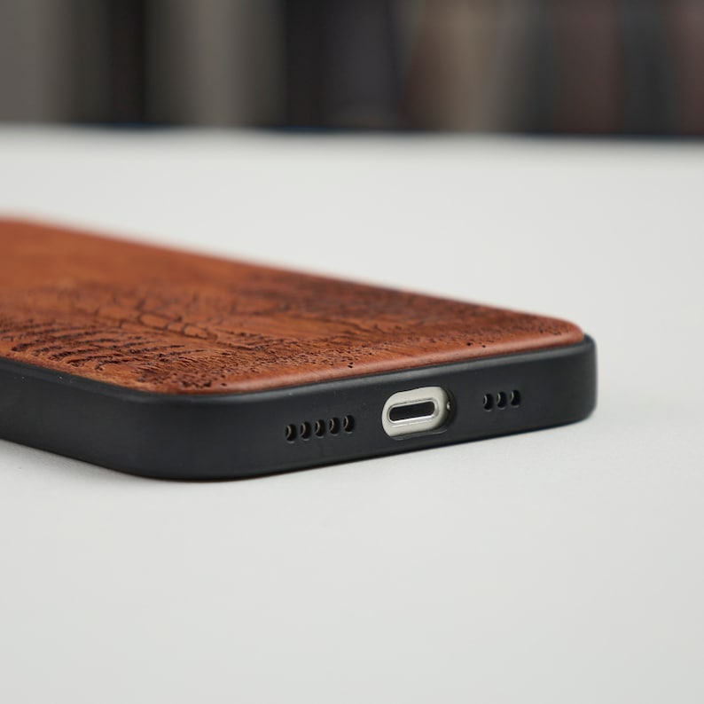 May include: A brown wood phone case with a black rubber bumper. The case has a cutout for the charging port and speaker.