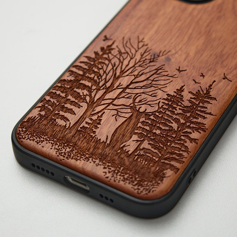 May include: A wooden phone case with a laser-engraved design of trees and birds. The case has a black rubber bumper.
