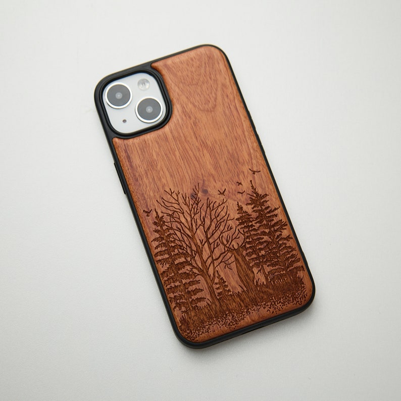May include: A brown wooden phone case with a laser-engraved design of trees and birds. The case has a black rubber bumper.