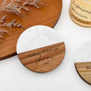 May include: Circular coaster with a white marble upper section and a wooden lower section. The wood is engraved with the names "Sewell & Callie", the name "shane", and the year "2026".