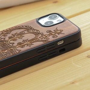 May include: A wooden phone case with a carved crown design. The case is brown and has a black protective bumper.