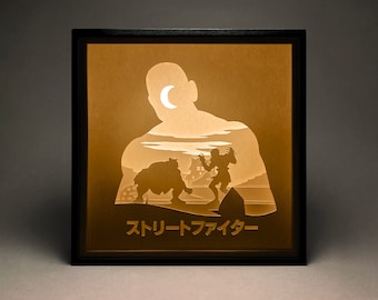 Peut inclure: Une œuvre d'art lumineuse encadrée en noir avec une silhouette d'un homme, d'une créature et d'un croissant de lune. Le texte "Street Fighter" est en bas de l'image.