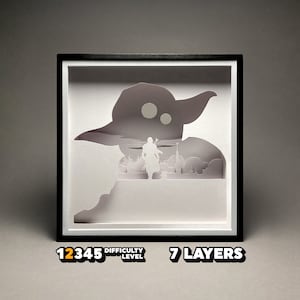 May include: A white papercraft model of a character from the Star Wars franchise, Yoda, with a figure of a Jedi Knight standing in front of him. The model is framed in a black frame with a white mat. The model is labeled "7 Layers" and "Difficulty Level 12345".