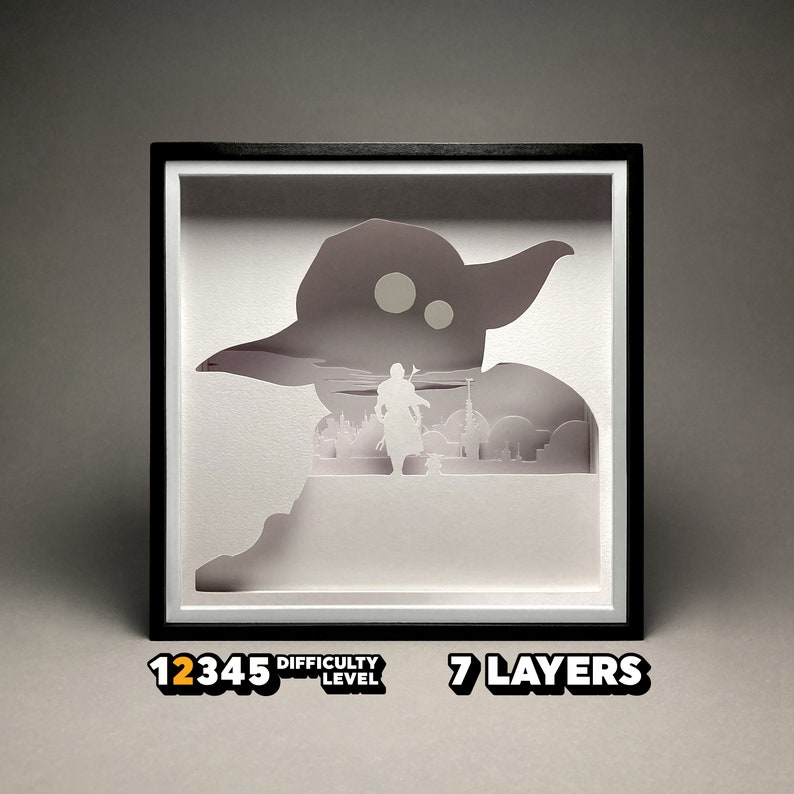 May include: A white papercraft model of a character from the Star Wars franchise, Yoda, with a figure of a Jedi Knight standing in front of him. The model is framed in a black frame with a white mat. The model is labeled "7 Layers" and "Difficulty Level 12345".