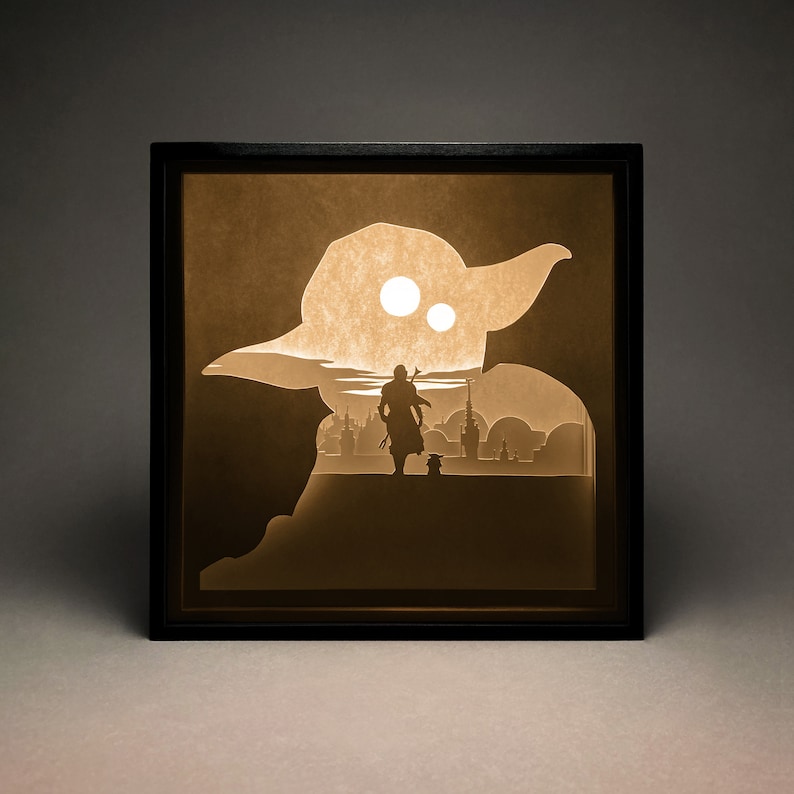 May include: A black framed shadow box with a paper cut-out design of a character from Star Wars standing in front of a cityscape. The character is holding a lightsaber and is looking towards the city. The background is a light brown color.