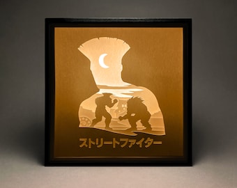 Peut inclure: Une œuvre d'art lumineuse encadrée de noir avec une silhouette d'une personne avec une crête et deux personnages qui se battent. Le texte "Street Fighter" est écrit en japonais en bas.