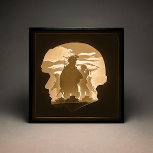 May include: A framed paper cut art piece depicting a silhouette of soldiers in a military scene. The soldiers are standing in front of a tank and are illuminated from behind, creating a dramatic effect.