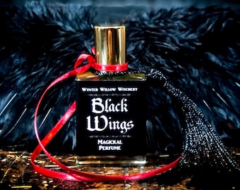 May include: A glass bottle of perfume with a gold cap and a black label that reads "Black Wings Magical Perfume" by Wynter Willow Witchery. The bottle is tied with a red ribbon and a black tassel.