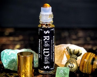 May include: A glass bottle of "$ Rich Witch $ Prosperity Oil" by White Willow Witchery. The bottle has a gold roller ball top and a black label with gold lettering. The bottle is surrounded by crystals and a gold money bag charm.