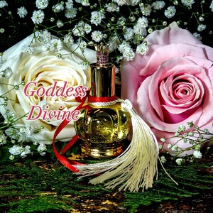 May include: A gold perfume bottle with a crown-shaped stopper and a white tassel. The bottle is surrounded by white and pink roses and small white flowers. The text "Goddess Divine" is written in pink letters on the image.