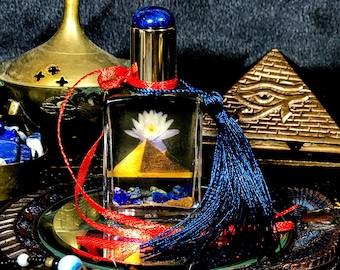 May include: A glass bottle with a blue and gold stopper, filled with a clear liquid and a white flower, a small golden pyramid, and blue stones. The bottle is tied with a red ribbon and a blue tassel.