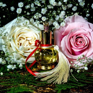 May include: A gold perfume bottle with a crown-shaped stopper and a white tassel, surrounded by white and pink roses and baby's breath.