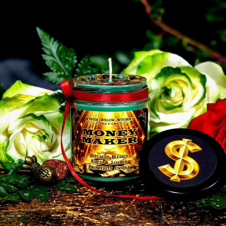 Puede incluir: Un tarro de vidrio verde con una vela, una cinta roja y una etiqueta dorada que dice "Money Maker -  Ritually Blessed Fixed & Loaded Prosperity Candle". La vela est&aacute; rodeada de rosas blancas y rojas y follaje verde. La tapa del tarro tiene un signo de d&oacute;lar dorado.