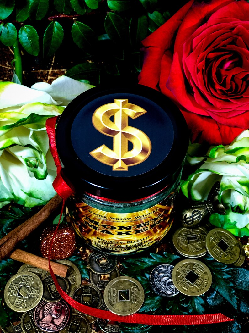 Puede incluir: Un tarro de vela negro con un signo de d&oacute;lar dorado en la tapa. El tarro est&aacute; rodeado de cinta roja, palitos de canela y monedas de oro. La vela est&aacute; etiquetada como "Money Make" y "White Willow Witchcraft".