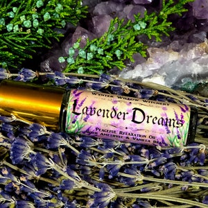 Puede incluir: Una peque&ntilde;a botella de vidrio con una tapa dorada y una etiqueta que dice "Lavender Dreams Peaceful Relaxation Oil with Amethyst & Vanilla Bean". La botella est&aacute; rodeada de flores de lavanda y cristales de amatista.