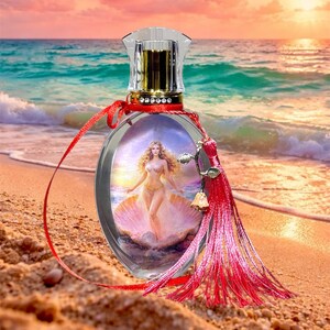 Puede incluir: Frasco de perfume ovalado con cuerpo de vidrio transparente y tap&oacute;n de cristal. La botella presenta una imagen de una mujer en una concha. Una cinta roja y una borla a&ntilde;aden un toque decorativo. El fondo muestra una escena de playa con una puesta de sol.