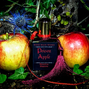 May include: A dark glass bottle with a gold top and a red tassel. The bottle is labeled "Winter Willow Witchery Poison Apple Magickal Perfume". Two red apples are in the background.