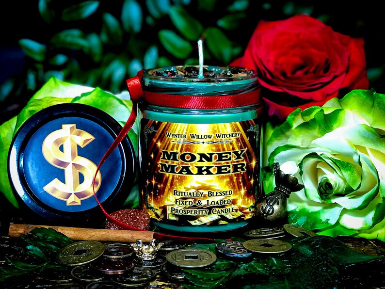 Puede incluir: Un tarro de vela de vidrio verde con una cinta roja y letras doradas que dicen "Money Maker" y "Ritually Blessed, Fixed & Loaded Prosperity Candle". La vela est&aacute; rodeada de monedas de oro, un palo de canela y rosas verdes y rojas.