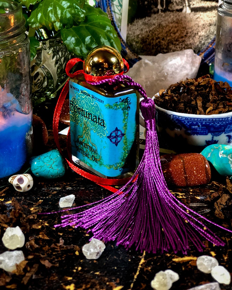 May include: A small bottle of blue and gold oil with a purple tassel. The bottle is labeled "Fortunata Ancestral Ritual Oil" and "Wynter Willow Witchery".