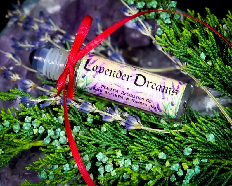 Puede incluir: Un peque&ntilde;o frasco de vidrio con rodillo con una cinta roja atada alrededor. El frasco est&aacute; etiquetado con "Lavender Dreams Peaceful Relaxation Oil with Amethyst & Vanilla Bean".