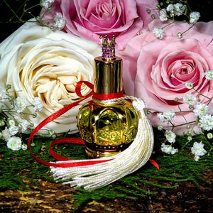May include: A gold perfume bottle with a crown-shaped stopper and a white tassel, surrounded by pink and white roses and baby's breath.