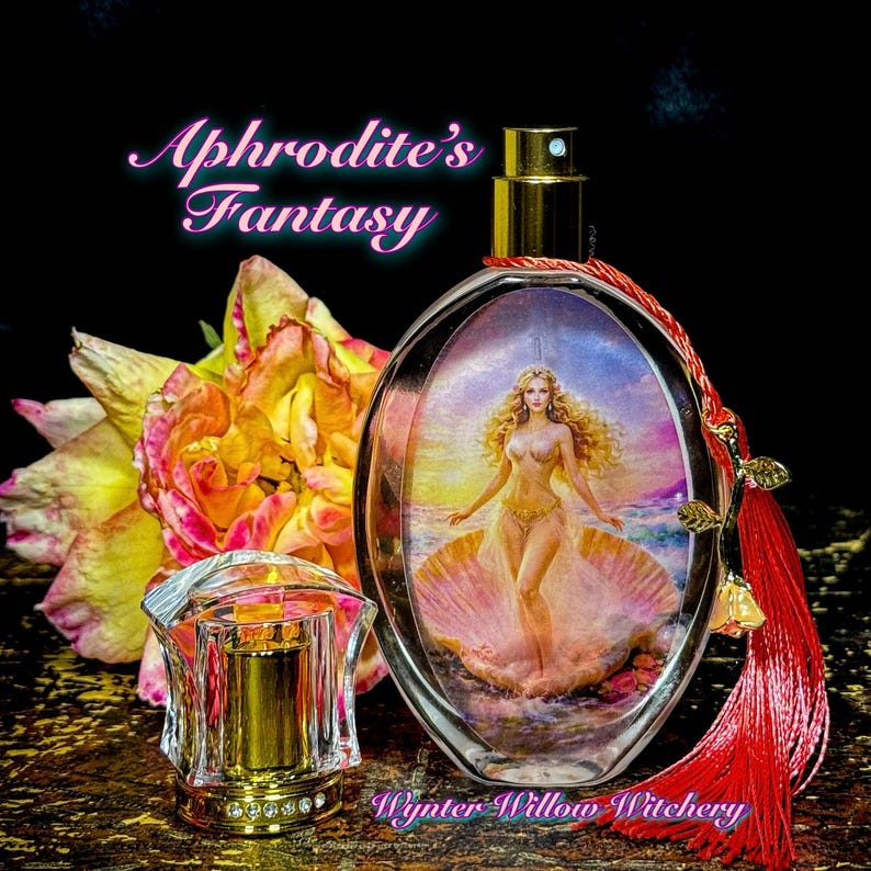 Puede incluir: Frasco de perfume ovalado con pulverizador dorado y pintura de una mujer en una concha. La botella lleva la etiqueta "Aphrodite's Fantasy" y tiene una borla roja. Un frasco de perfume transparente con adornos dorados se encuentra frente a una rosa amarilla y rosa.