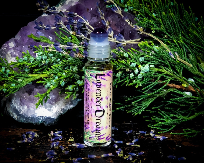 Puede incluir: Una peque&ntilde;a botella de vidrio con un aplicador de bola. La botella est&aacute; etiquetada con "Lavender Dreams" y "Winter Willow Witchery." La botella est&aacute; rodeada de flores de lavanda y un cristal morado.