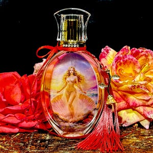 Puede incluir: Frasco de perfume ovalado con tapa de cristal transparente y borde dorado. La botella presenta una imagen de una mujer en una concha. Una cinta roja y una borla adornan la botella. Rosas rojas y amarillas en el fondo.
