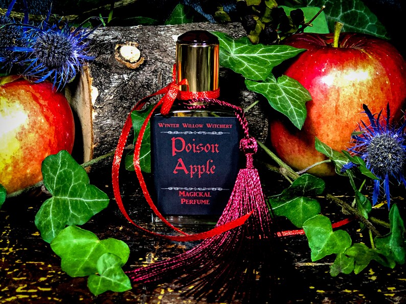 May include: A small bottle of perfume with a black label that reads "Winter Willow Witchery Poison Apple Magical Perfume". The bottle is tied with a red ribbon and a red tassel. The bottle is surrounded by red apples, green leaves, and blue flowers.
