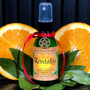 May include: A green glass bottle with a red ribbon and a gold pentagram charm. The bottle is labeled "WINTER WILLOW WITCHERY Revitalize A MAGICKAL BERGAMOT & FRANKINCENSE MIST BLESSED WITH CITRINE SUNSTONE & BAY LAUREL".