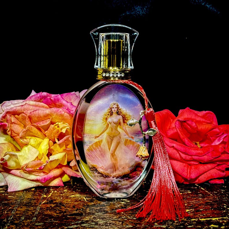 Puede incluir: Un frasco de perfume ovalado con tapa dorada y una imagen decorativa de una mujer en una concha. El frasco tiene una borla roja y est&aacute; rodeado de rosas rosas y rojas. El fondo es negro.