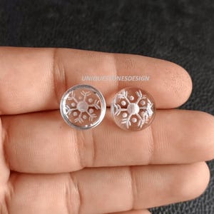 May include: Pair of clear glass snowflake earrings. The earrings are round and have a silver snowflake design etched into the glass.