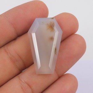 Op de afbeelding: Een witte agaat edelsteen met bruine dendritische insluitsels, gesneden in de vorm van een kist. De edelsteen is ongeveer 5 cm lang en 2,5 cm breed.