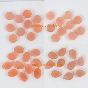 May include: Assortment of 18 pink and orange gemstone cabochons in round, oval, and teardrop shapes. The stones are smooth and polished, with a translucent appearance.  The text "uniquestonesdesign" appears twice in the image.