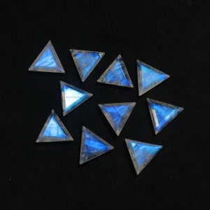 May include: Ten triangular iridescent moonstone cabochons with a blue sheen on a black background.