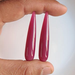 May include: Two teardrop-shaped cabochons of pink agate, each with a smooth, polished surface.