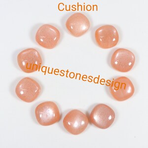 May include: Ten peach-coloured gemstone cabochons arranged in a circle on a white surface. The cabochons are all the same size and shape, and they have a smooth, polished finish. The text "Cushion" is written above the cabochons, and the text "uniquestonesdesign" is written below the cabochons.