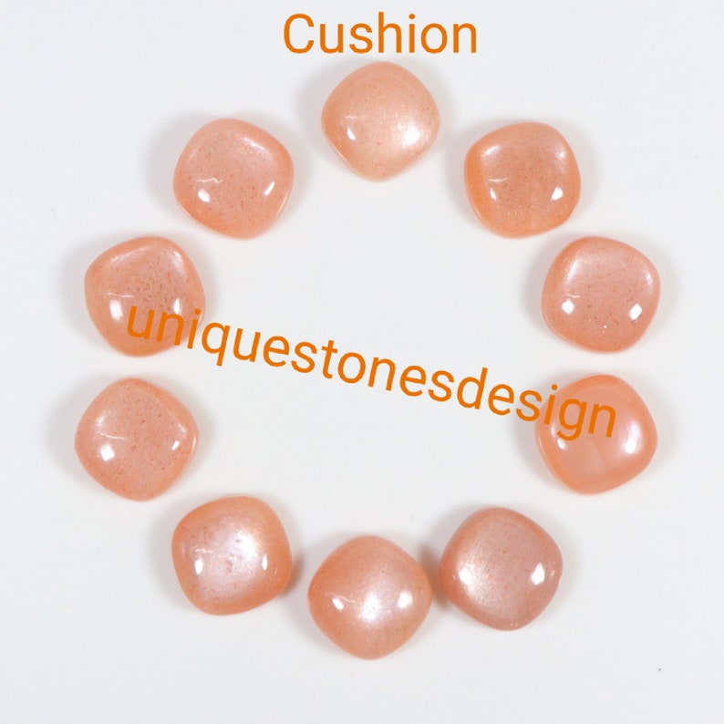 May include: Ten peach-coloured gemstone cabochons arranged in a circle on a white surface. The cabochons are all the same size and shape, and they have a smooth, polished finish. The text "Cushion" is written above the cabochons, and the text "uniquestonesdesign" is written below the cabochons.