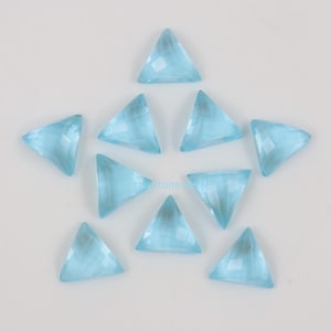 Può includere: Una collezione di dieci gemme triangolari azzurro chiaro, disposte a forma di stella. Ogni gemma ha una superficie sfaccettata, che cattura la luce e mostra una sottile scintilla. Le gemme sono su sfondo bianco.