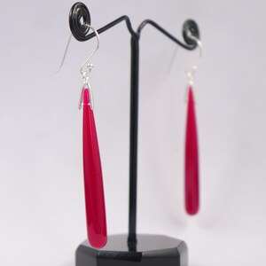 May include: A pair of dangle earrings with a teardrop-shaped, bright pink stone. The earrings are made of silver and have a hook closure.
